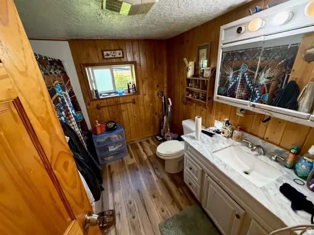 Bathroom featuring wood-finish wall paneling, a single vanity with a white countertop and integrated sink, a mirrored medicine cabinet, a window, and wood-finish flooring