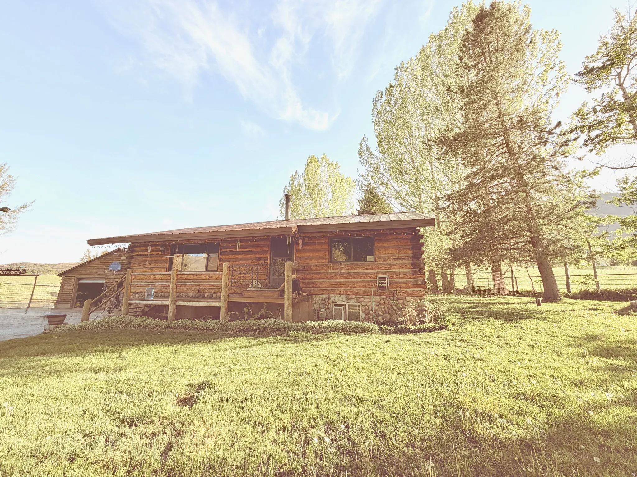 Log cabin exterior featuring a covered porch, stone foundation, metal roof, and a gravel driveway