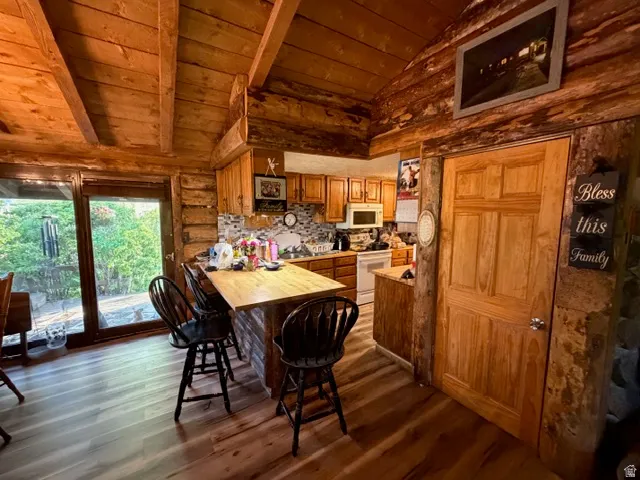 Kitchen area featuring natural wood cabinetry, wood-finish flooring, a built-in breakfast bar, and a patterned tile backsplash