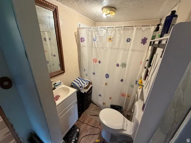Compact bathroom featuring a shower stall, a single vanity with a white basin sink, and wood-finish flooring