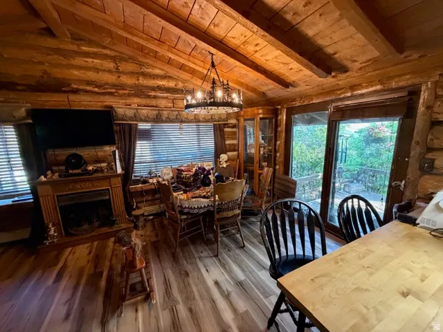 Vaulted wood-beamed ceilings with a wagon wheel chandelier, wood-finish flooring, a fireplace with a wood mantel, and glass sliding doors opening to an outdoor deck