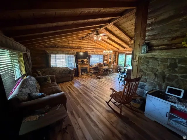 Spacious interior featuring wood-finish flooring, exposed wood beam ceilings, log walls, stone-faced fireplace, and multiple windows with blinds