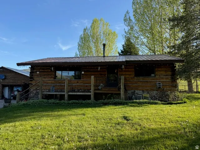 Log cabin exterior featuring a metal roof, a stone foundation, a covered porch with a wood railing, and a detached garage structure