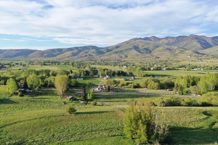 Expansive rural landscape featuring distant mountains, verdant fields, and scattered mature trees