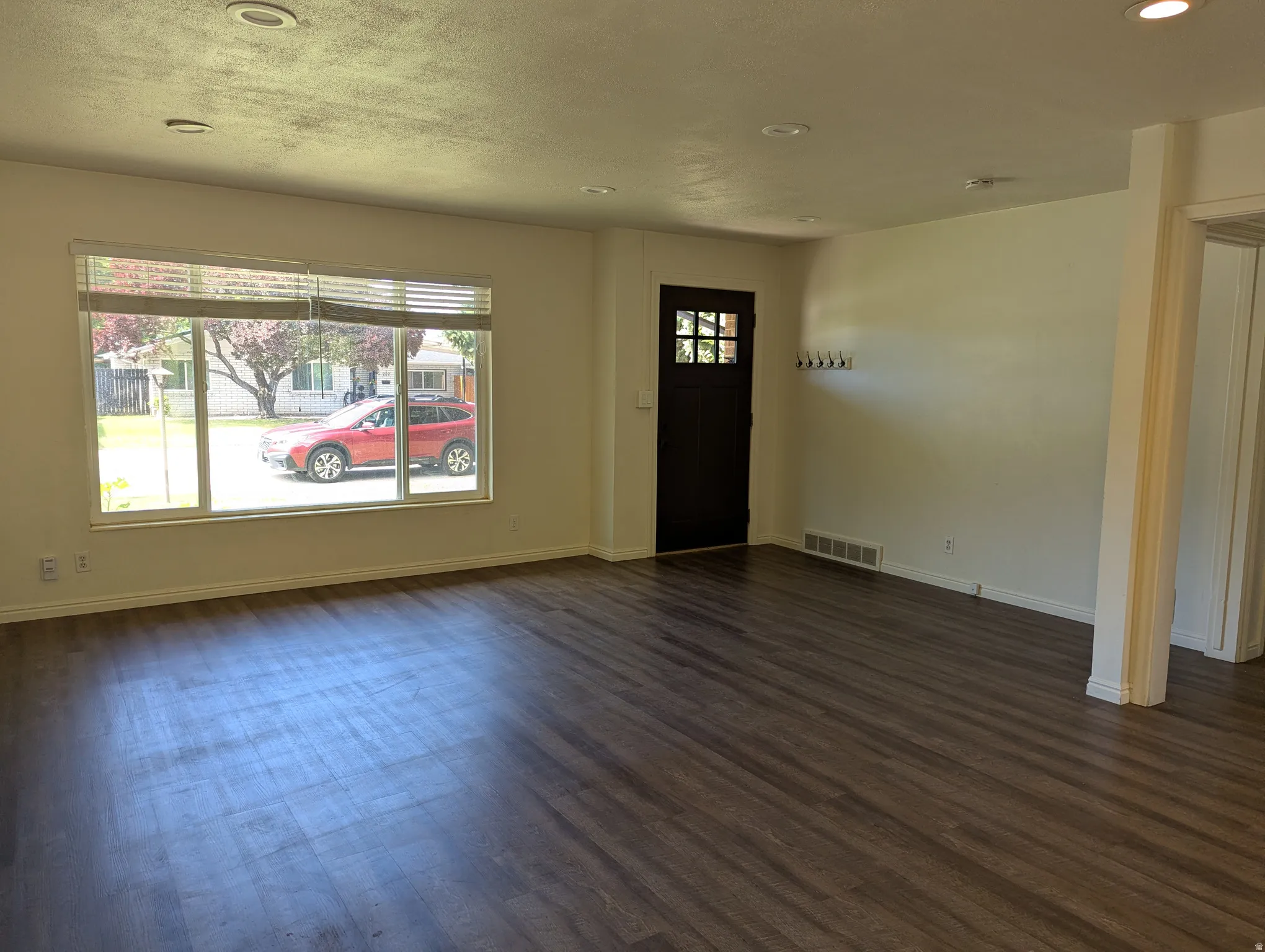 Spacious open living room featuring  laminate wood-finish flooring, a large picture window, recessed lighting, and a dark-paneled entry door with decorative glass inserts