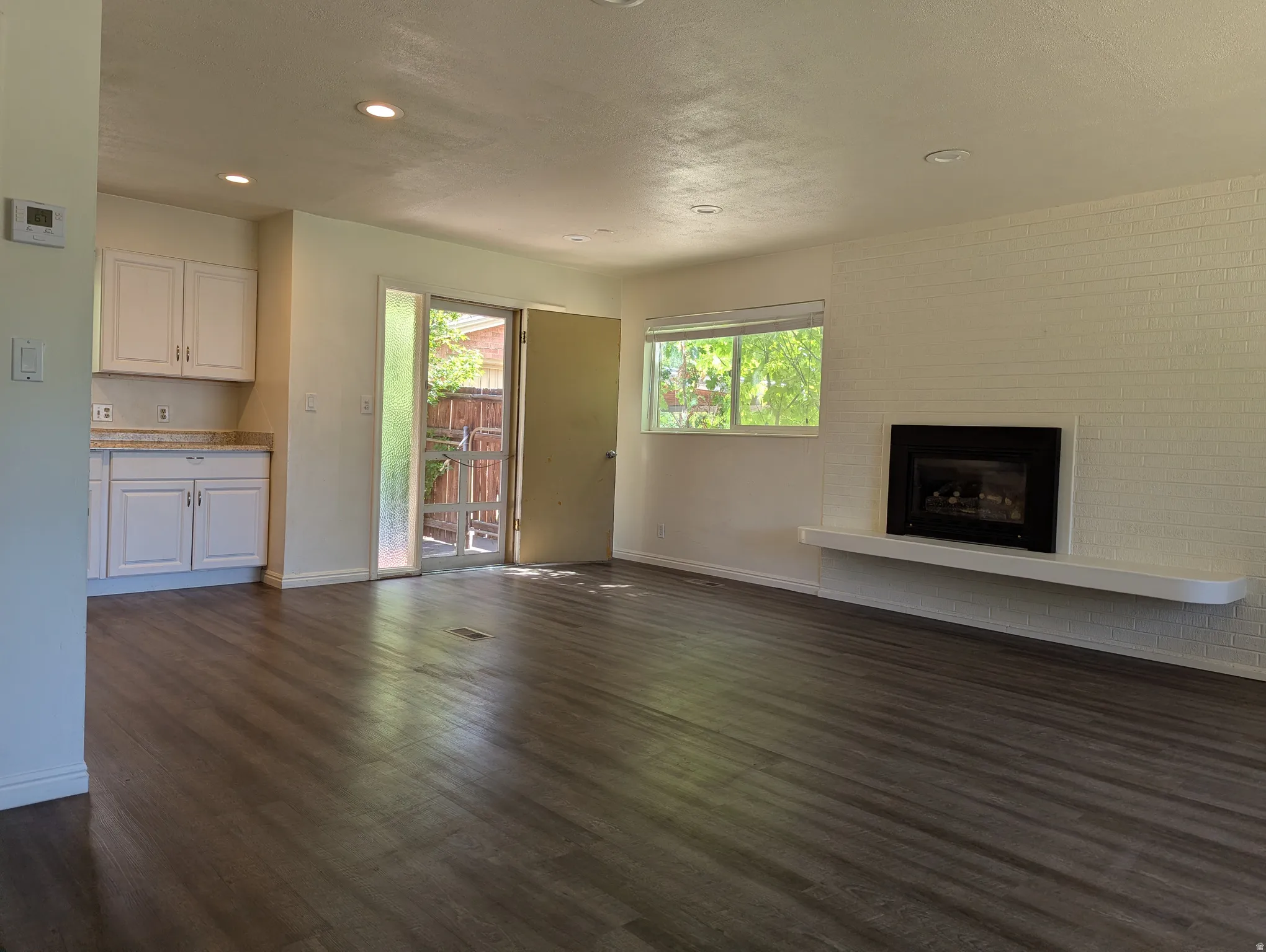 Spacious living area featuring laminate wood-finish flooring, a contemporary fireplace with a floating mantel, and a dedicated kitchen nook with white cabinetry and a stone-look countertop