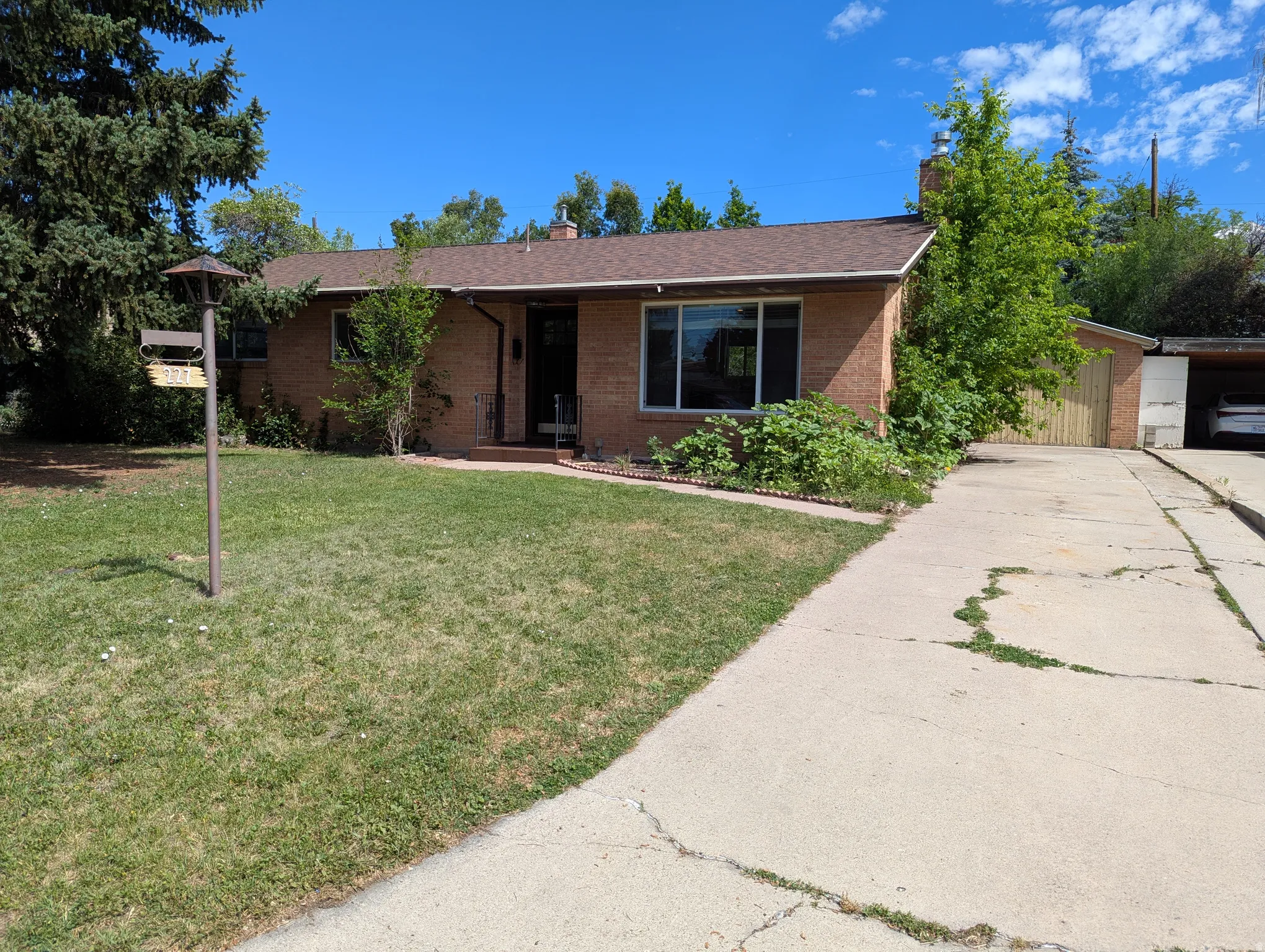 Brick exterior featuring a two-car driveway, 1-car garage and mature landscaping
