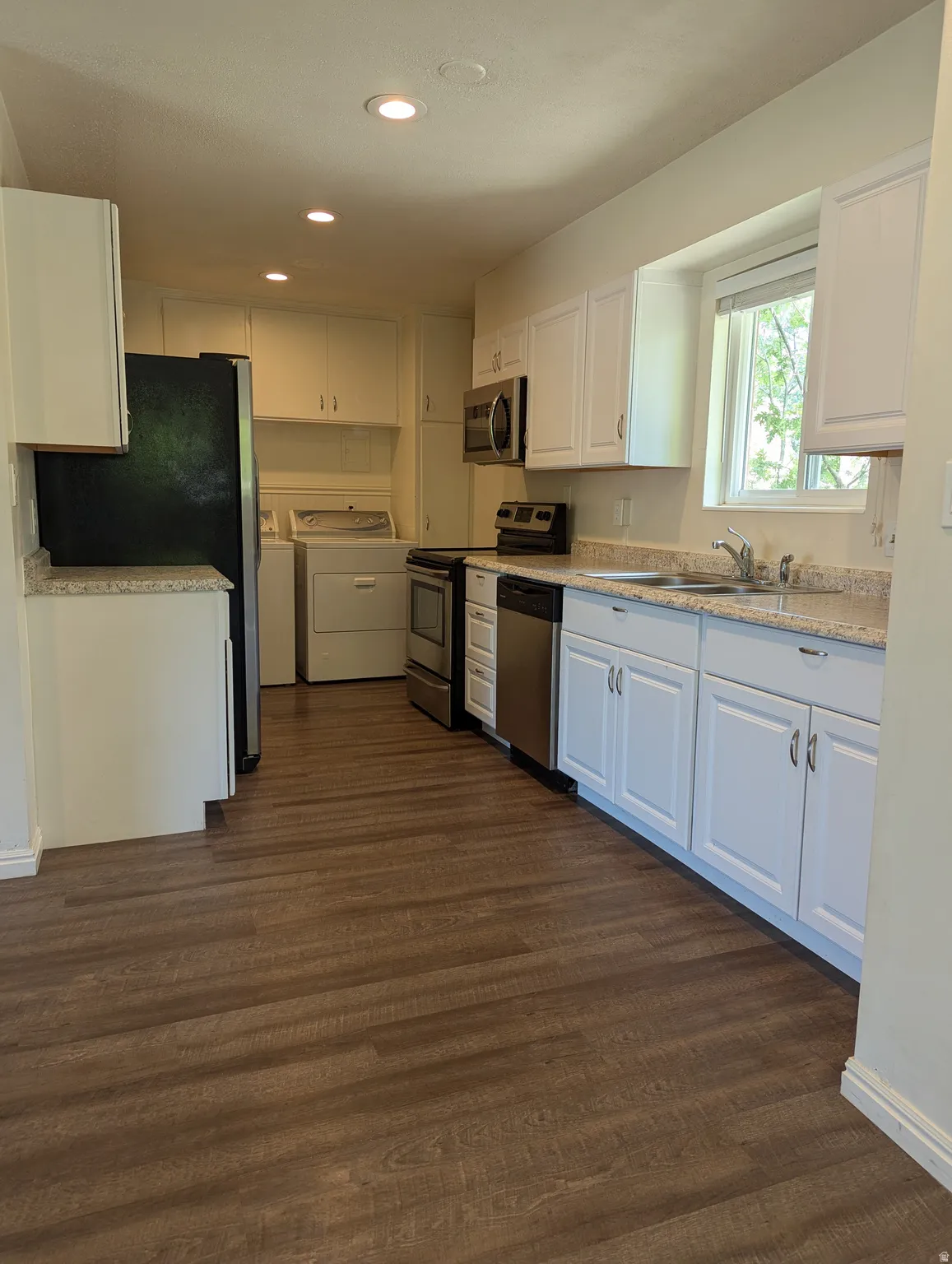 Open-concept kitchen featuring laminate wood-finish flooring, white cabinetry, speckled stone-look countertops, and stainless steel appliances