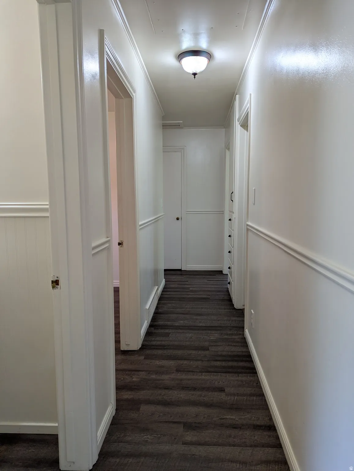 Hallway featuring laminate wood-finish flooring, white wainscoting, white crown molding, and a flush-mount ceiling light fixture
