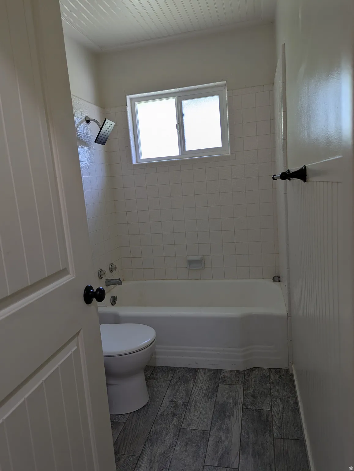 Full bathroom featuring a white bathtub, ceramic wall tiling, laminate wood-finish flooring.