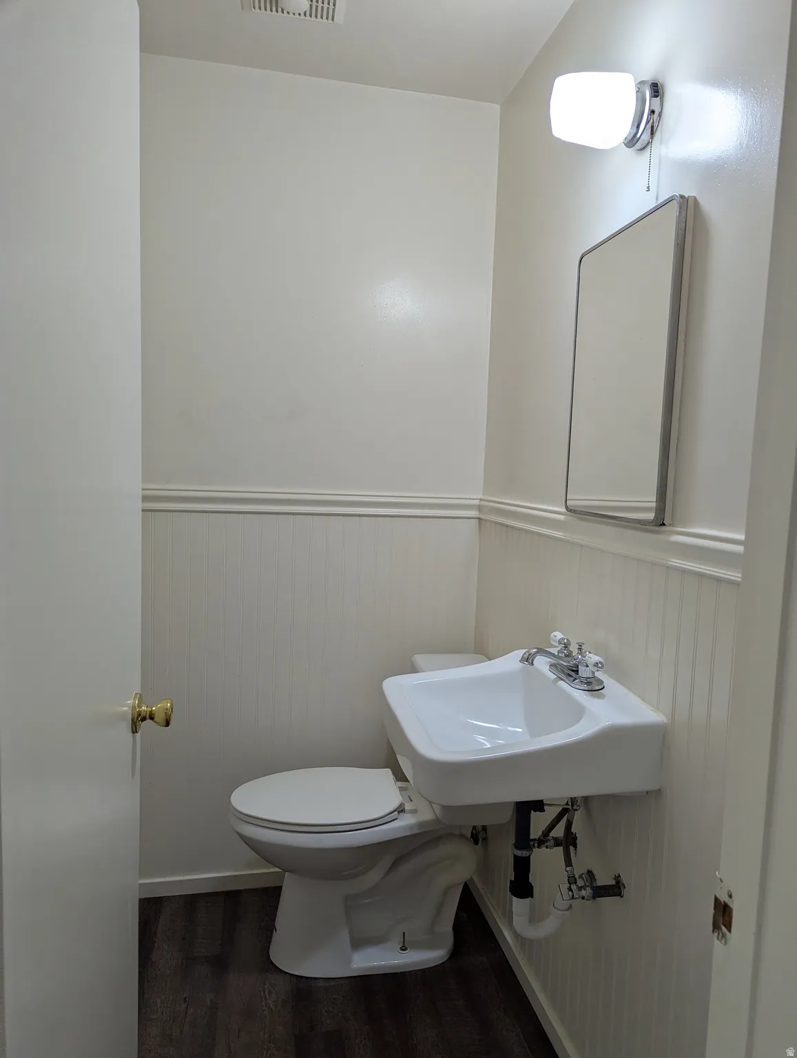 Compact powder room featuring a wall-mounted sink with chrome faucet, white toilet, and laminate wood-finish flooring