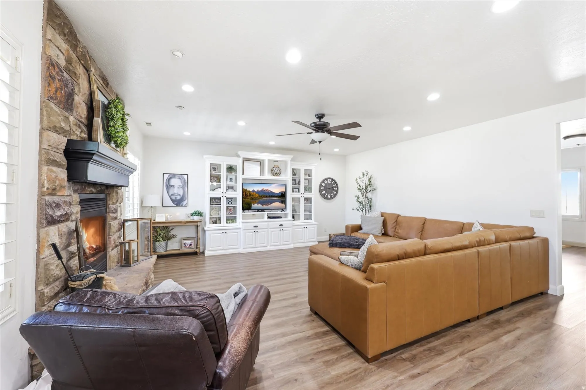 Spacious living area featuring a stone fireplace with a black mantel, recessed lighting, wood-finish flooring, and a ceiling fan