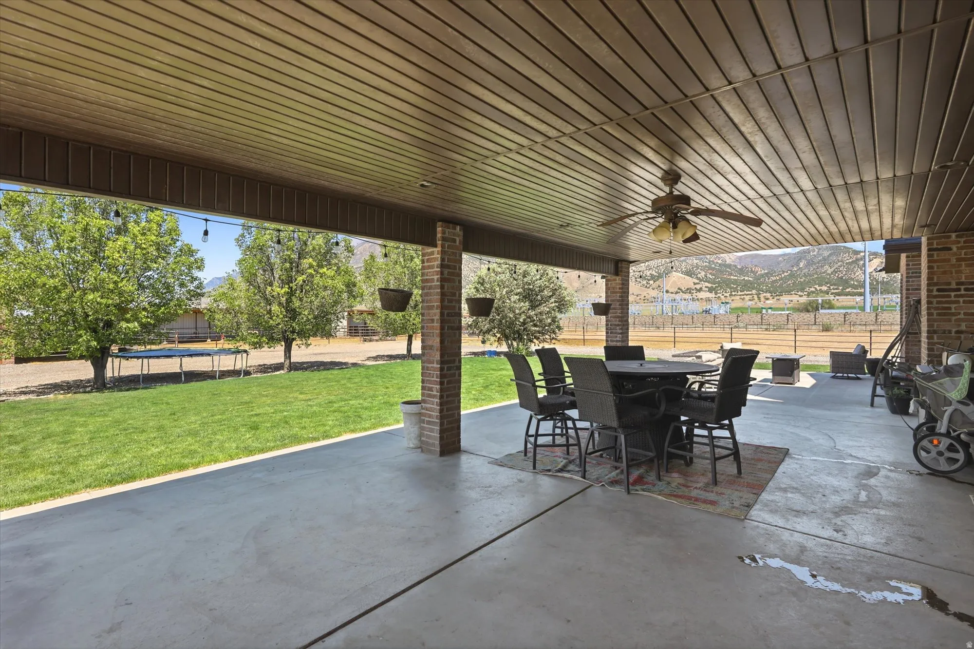 Expansive covered patio featuring a wood-panel ceiling, ceiling fan, and brick support columns