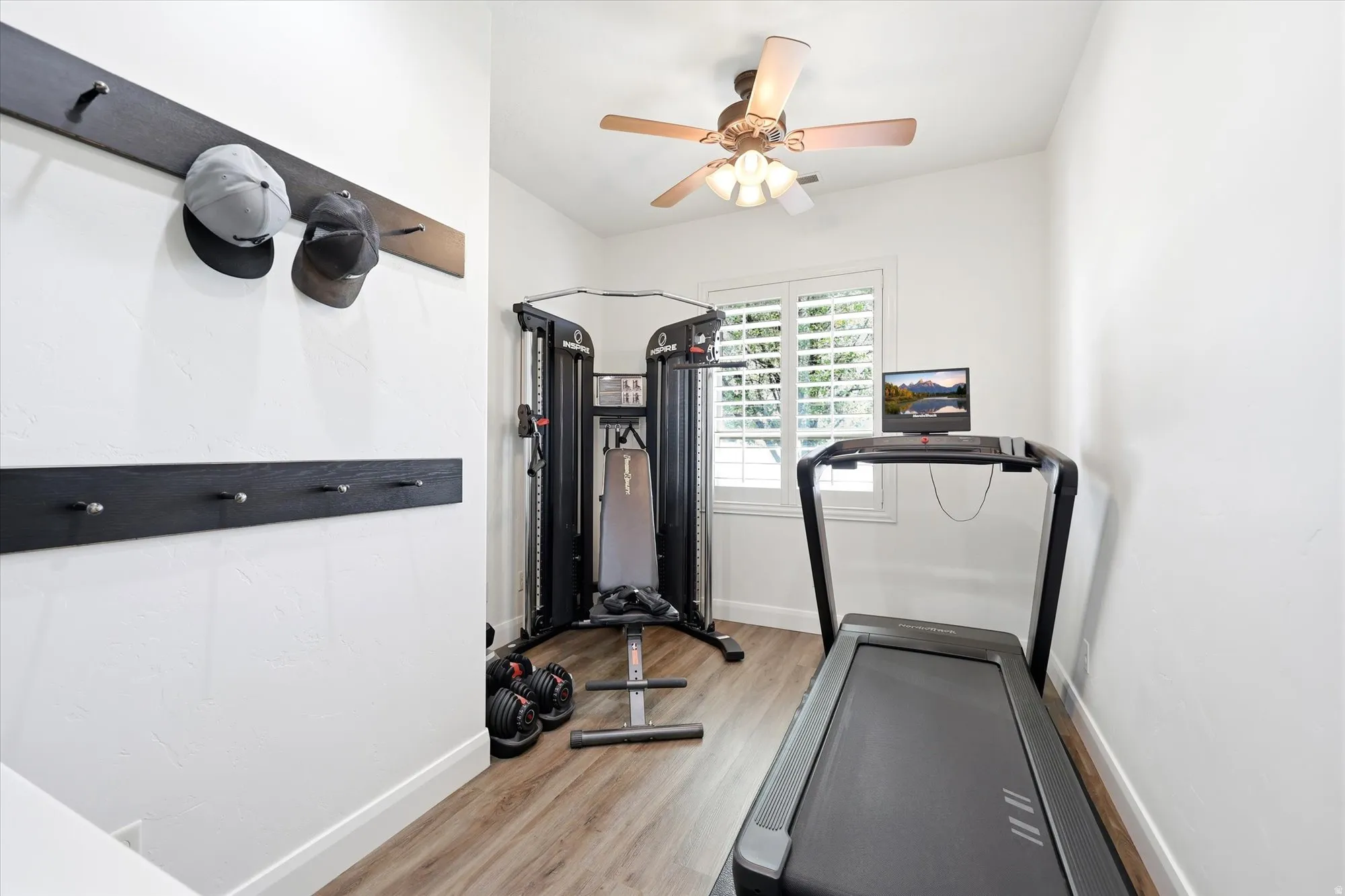 Bright room featuring wood-finish flooring, a ceiling fan with integrated lighting, and a window with plantation shutters