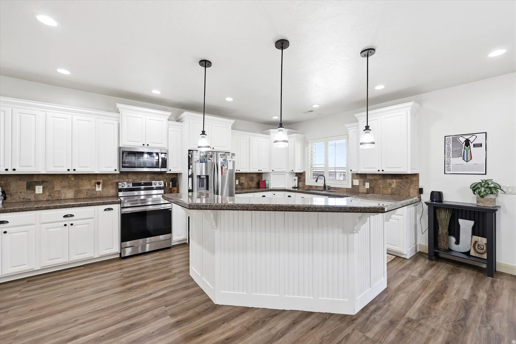 Kitchen featuring a central island with beadboard paneling, white cabinetry, dark speckled countertops, stainless steel appliances, and wood-finish flooring