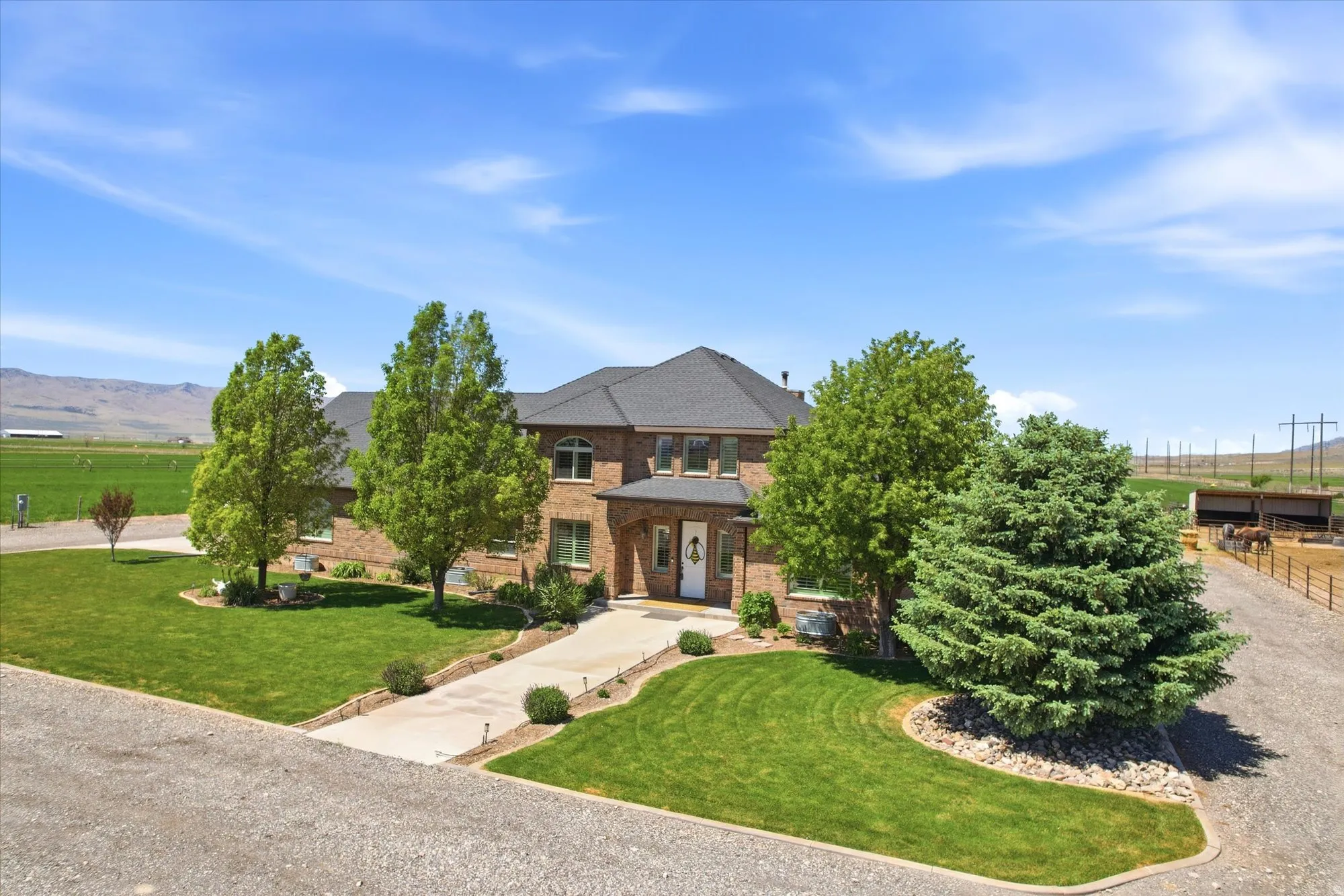 Brick exterior residence with a dark shingle roof, arched windows, manicured lawn, and mature trees