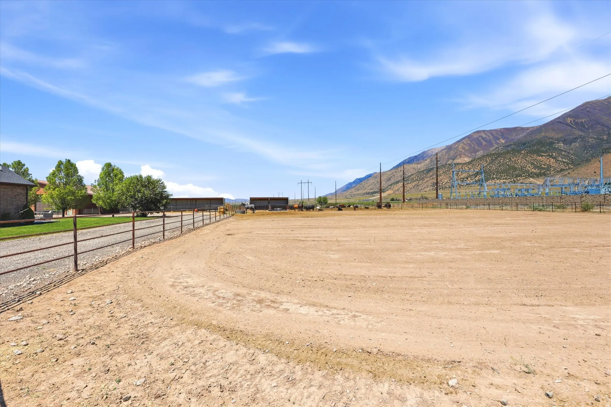 Expansive dirt lot with a metal pipe fence bordering a gravel drive and grass area