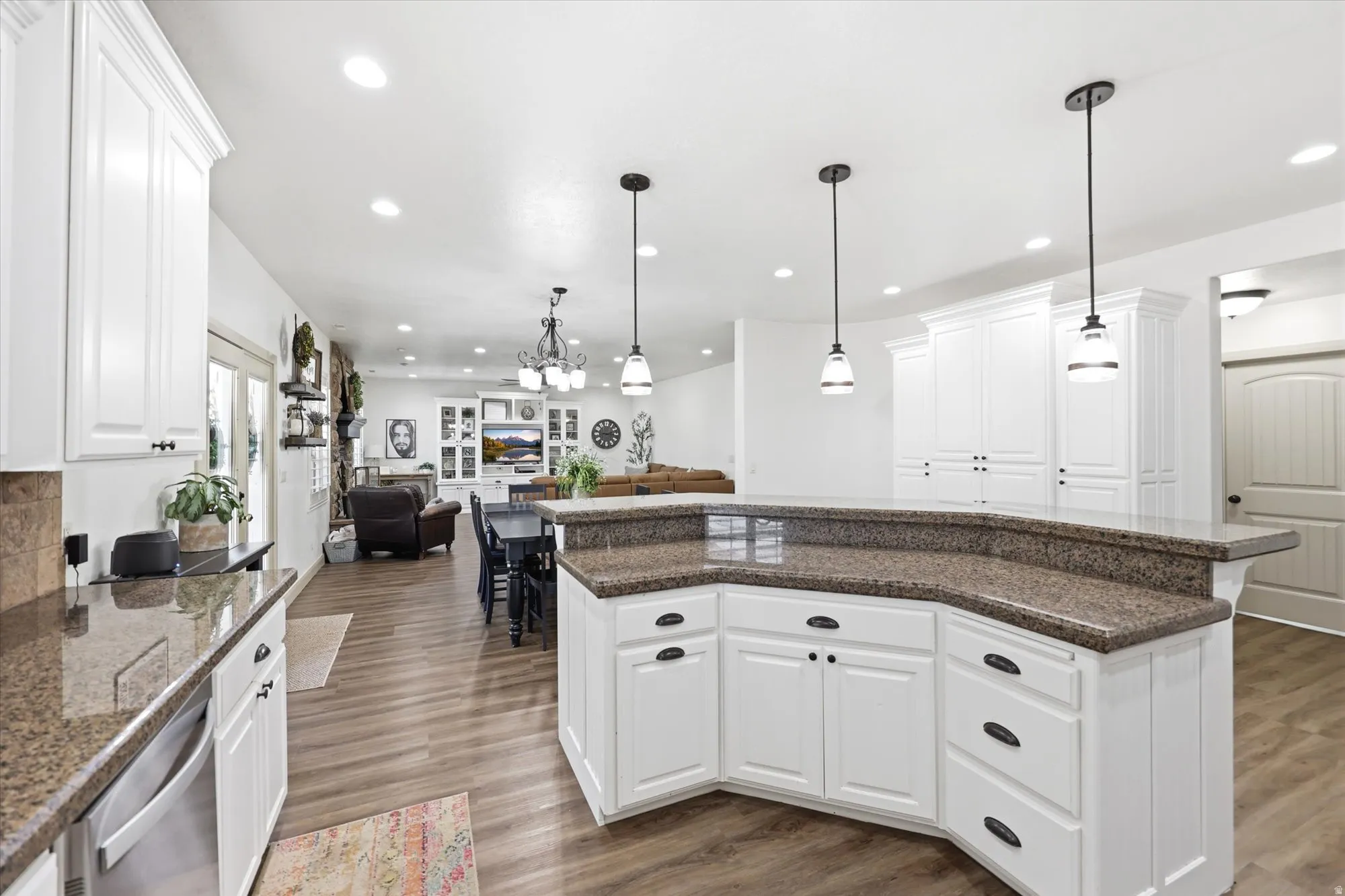 Kitchen featuring white cabinetry with dark hardware, a spacious granite-finish island, two pendant lights, recessed lighting, and wood-finish flooring