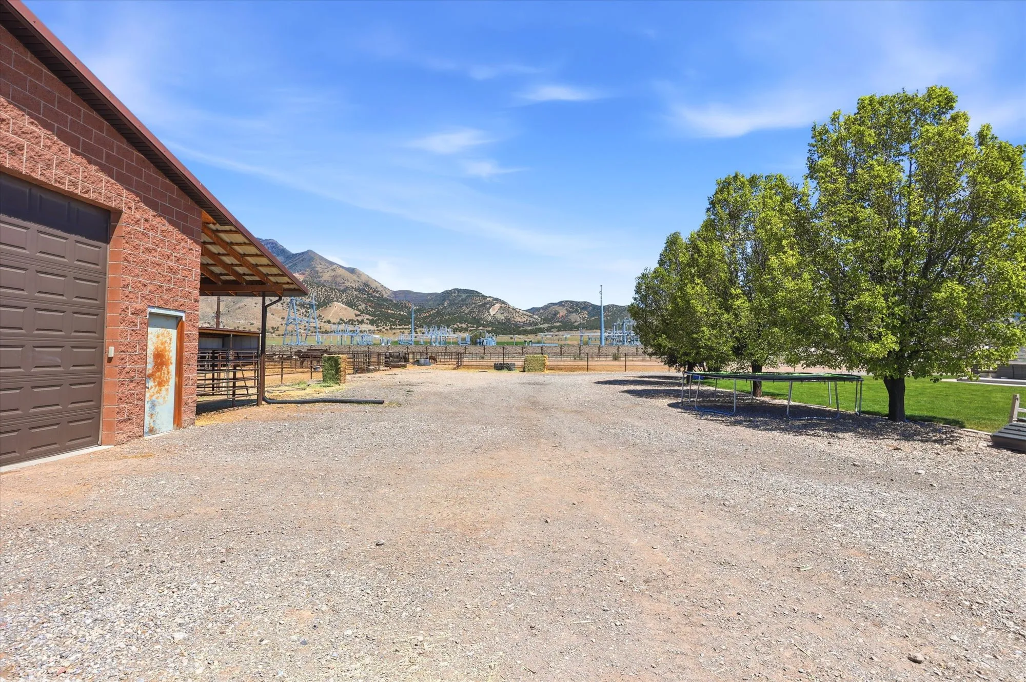 Gravel driveway with a red brick building featuring a large garage door, covered outdoor area, and mountain scenery