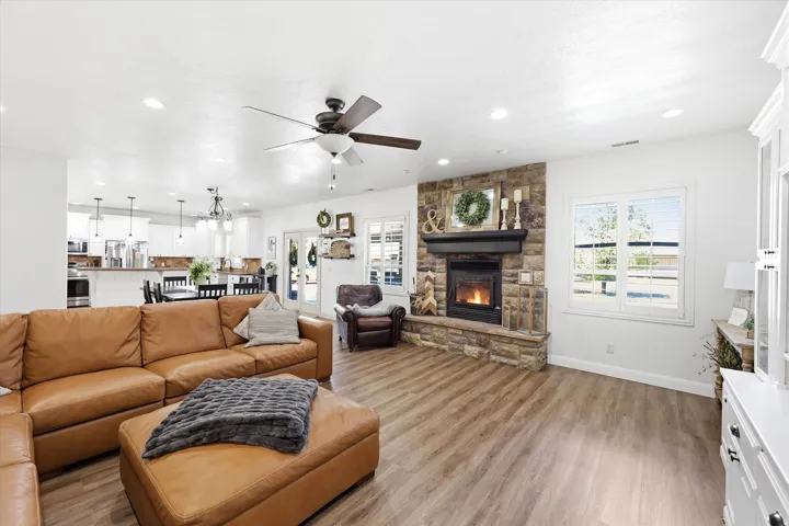 Open-concept living space featuring wood-finish flooring, a stone-faced fireplace with a dark wood mantel, recessed lighting, and a ceiling fan