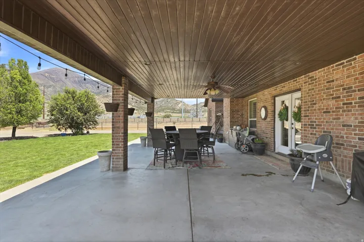 Expansive covered patio featuring a concrete surface, brick pillars, a wood-slat ceiling, string lighting, and a ceiling fan
