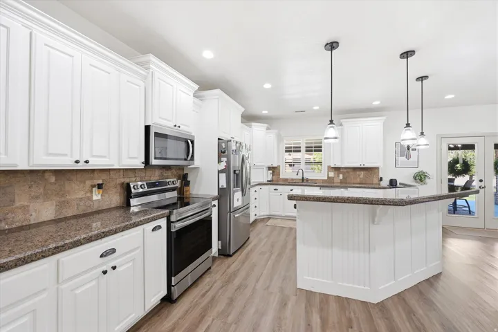 Kitchen featuring white cabinetry, stone-finish countertops, stainless steel appliances, a tiled backsplash, and wood-finish flooring