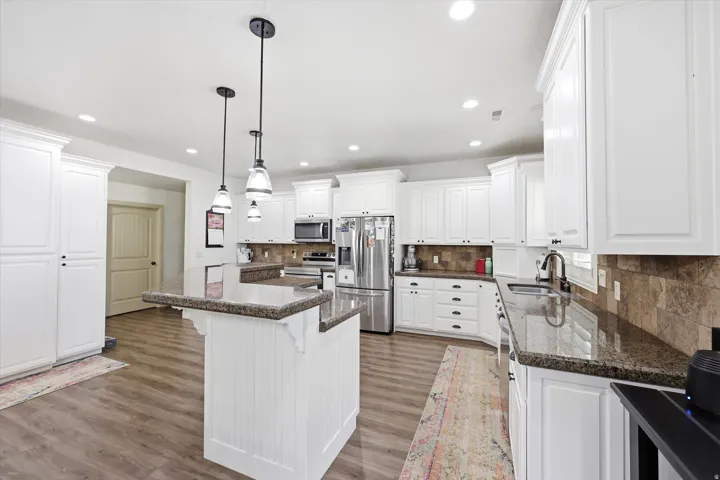 Bright kitchen featuring white cabinetry, granite countertops, stainless steel appliances, a tiled backsplash, and wood-finish flooring