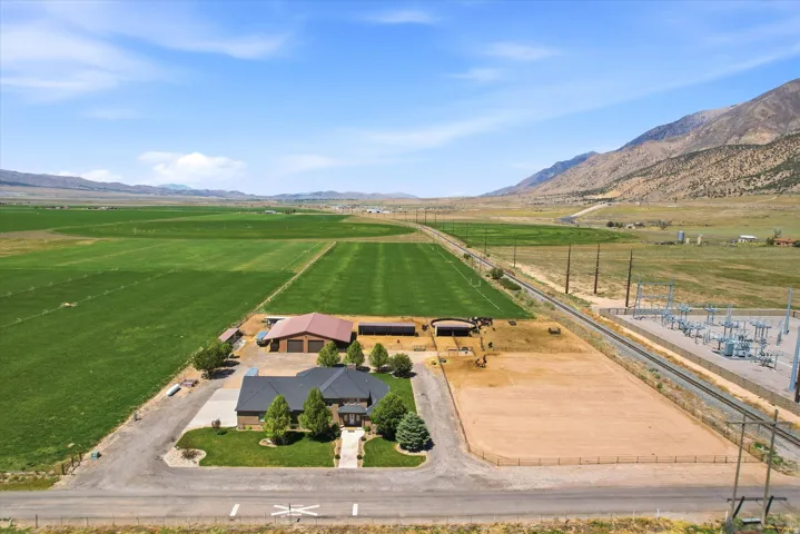 LAND BEHIND AVAILABLE SEPARATELY Expansive property featuring a central residence with an attached garage, a separate large outbuilding with a red roof, a substantial agricultural field, and distant mountain backdrops