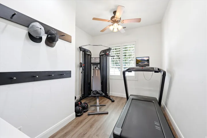 Bright room featuring wood-finish flooring, a ceiling fan with integrated lighting, and a window with plantation shutters