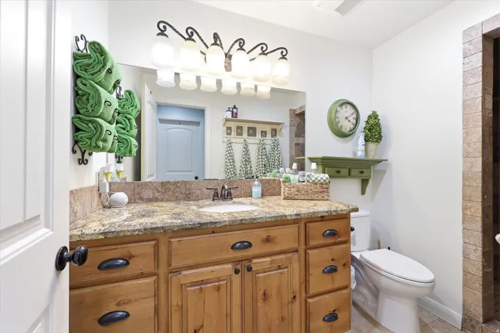 PRIMARY Bathroom featuring a light wood vanity with multiple drawers and cabinet storage, a stone-finish countertop, a single basin sink, and a large wall-mounted mirror