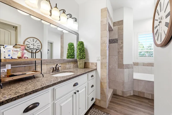 PRIMARY Bathroom featuring a spacious vanity with a granite countertop, white cabinetry with dark hardware, an undermount sink, and a large mirror with a rustic-style light fixture