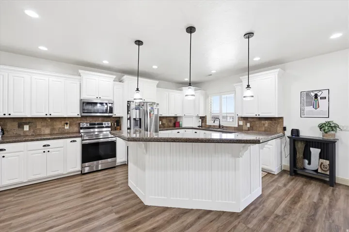 Kitchen featuring a central island with beadboard paneling, white cabinetry, dark speckled countertops, stainless steel appliances, and wood-finish flooring