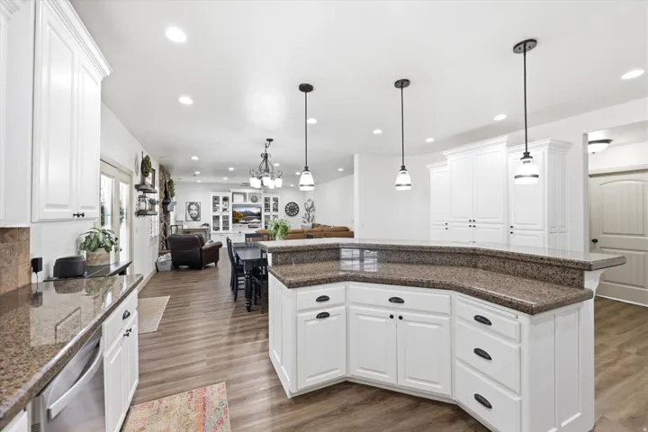Kitchen featuring white cabinetry with dark hardware, a spacious granite-finish island, two pendant lights, recessed lighting, and wood-finish flooring