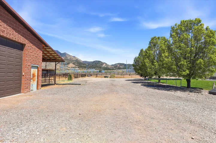 Gravel driveway with a red brick building featuring a large garage door, covered outdoor area, and mountain scenery
