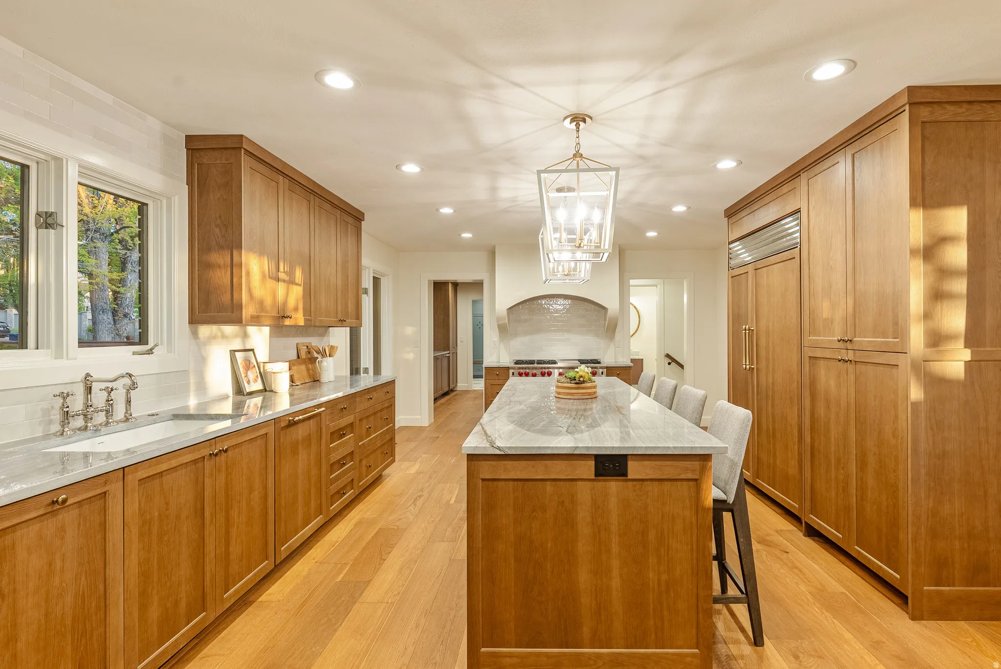 Open-concept kitchen featuring light wood cabinetry, a large center island with seating, recessed lighting, and a decorative pendant light fixture