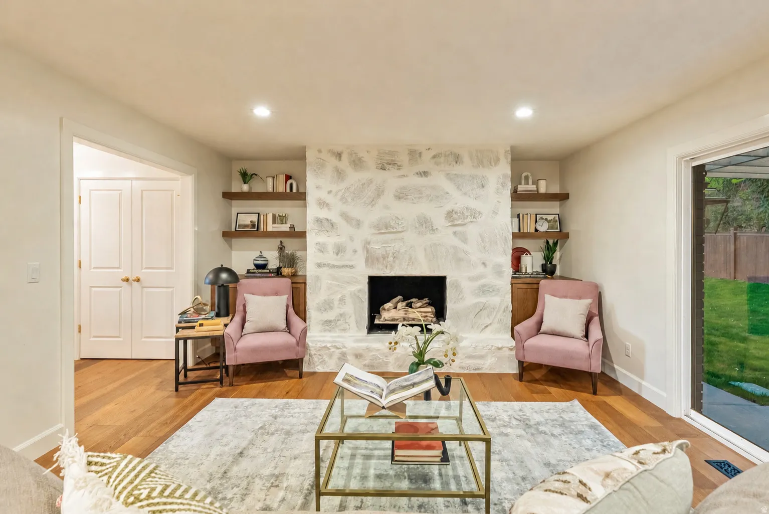 Living area featuring a stone-clad fireplace with a hearth, wood-finish flooring, recessed lighting, and a sliding glass door opening to a green lawn