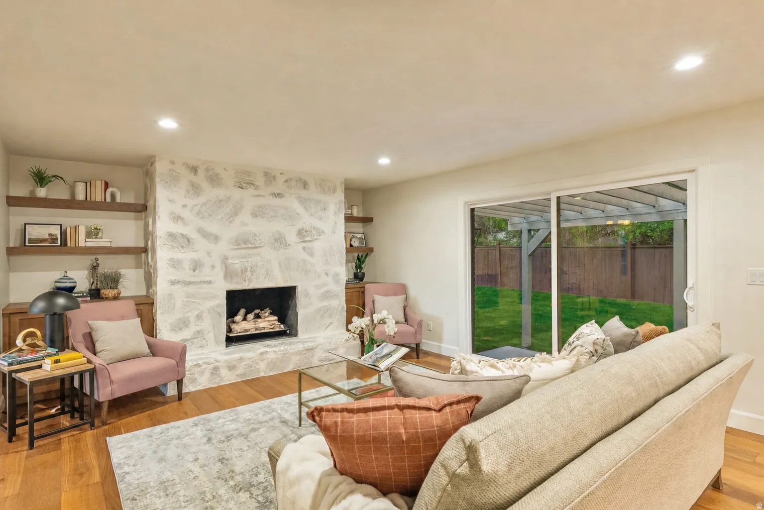 Spacious living area featuring a stone fireplace, wood-finish flooring, recessed lighting, and built-in floating shelves