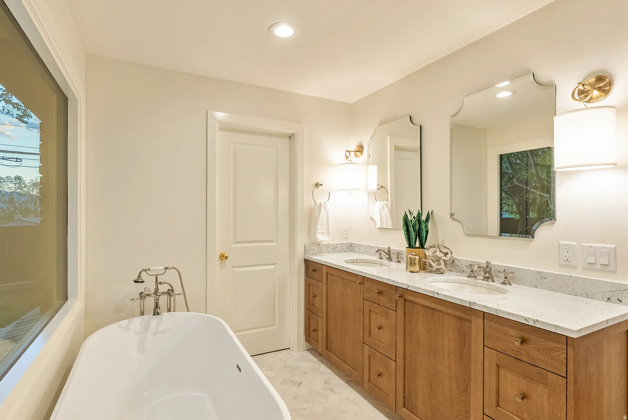 Freestanding soaking tub with floor-mounted faucet, dual vanities with undermount sinks, and stone countertops