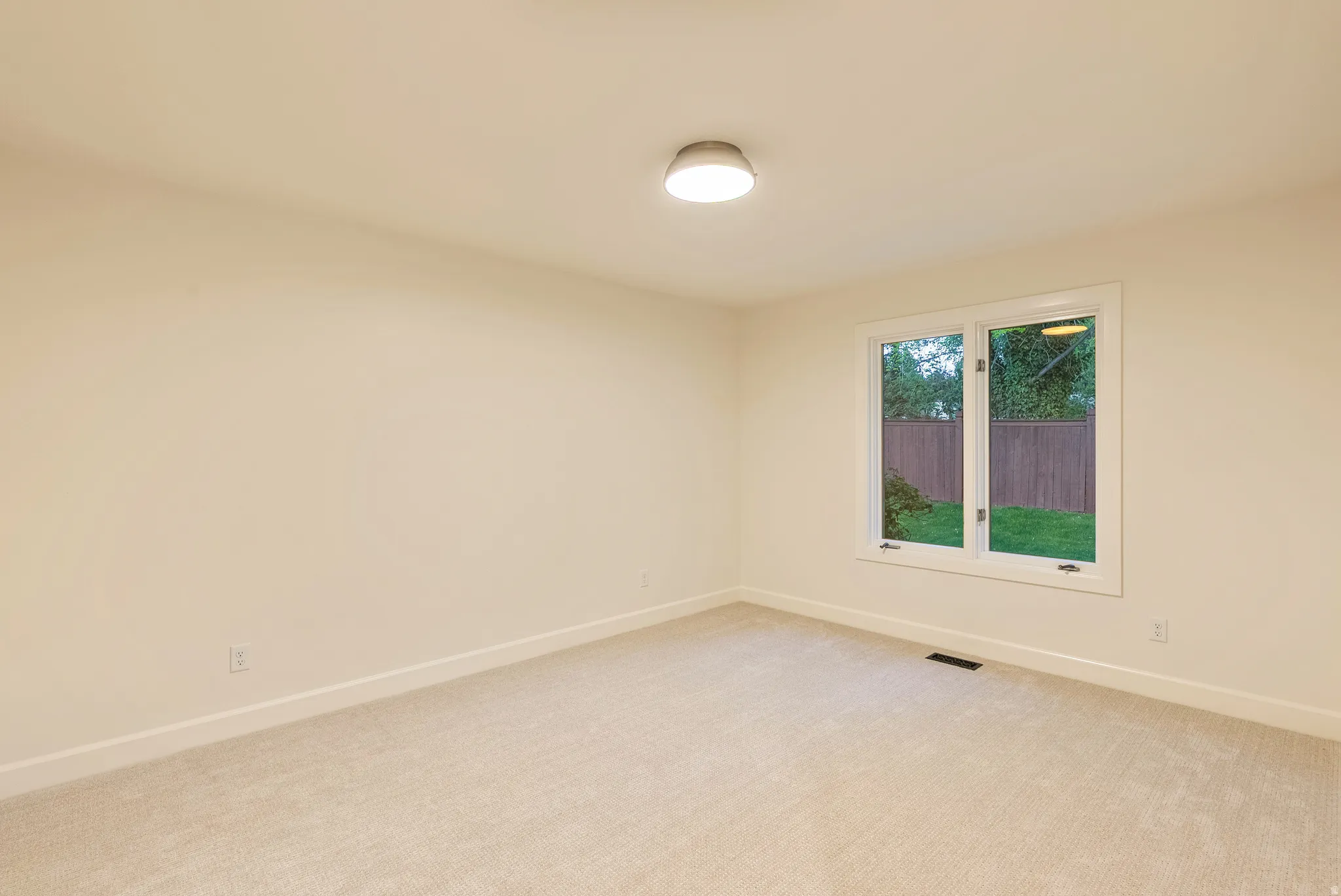 Neutral-toned room featuring a single window, plush carpeting, and a flush-mount ceiling light fixture