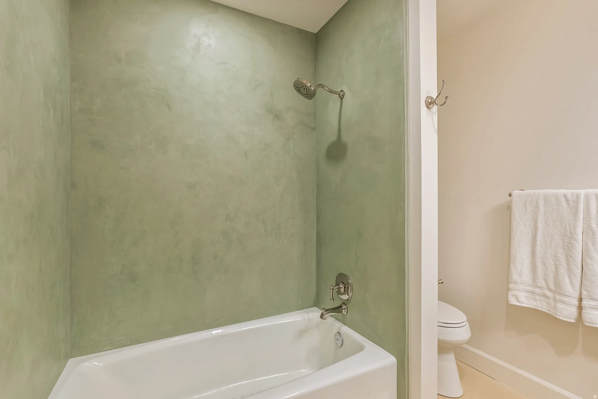Bathtub and shower combination featuring textured green walls and brushed nickel fixtures