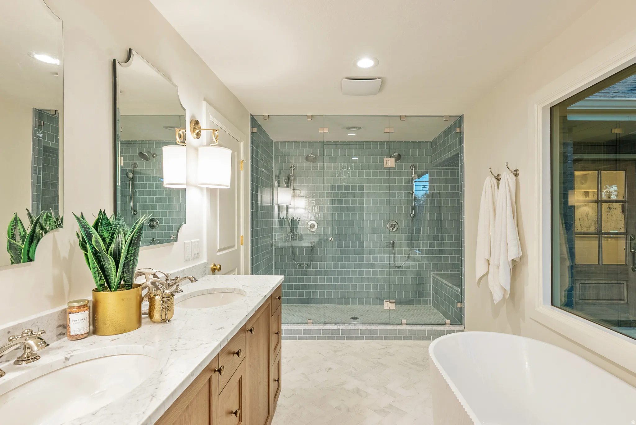 Spacious bathroom featuring a frameless glass shower enclosure with subway tile, a freestanding soaking tub, a double vanity with stone countertops, and wood-finish cabinetry