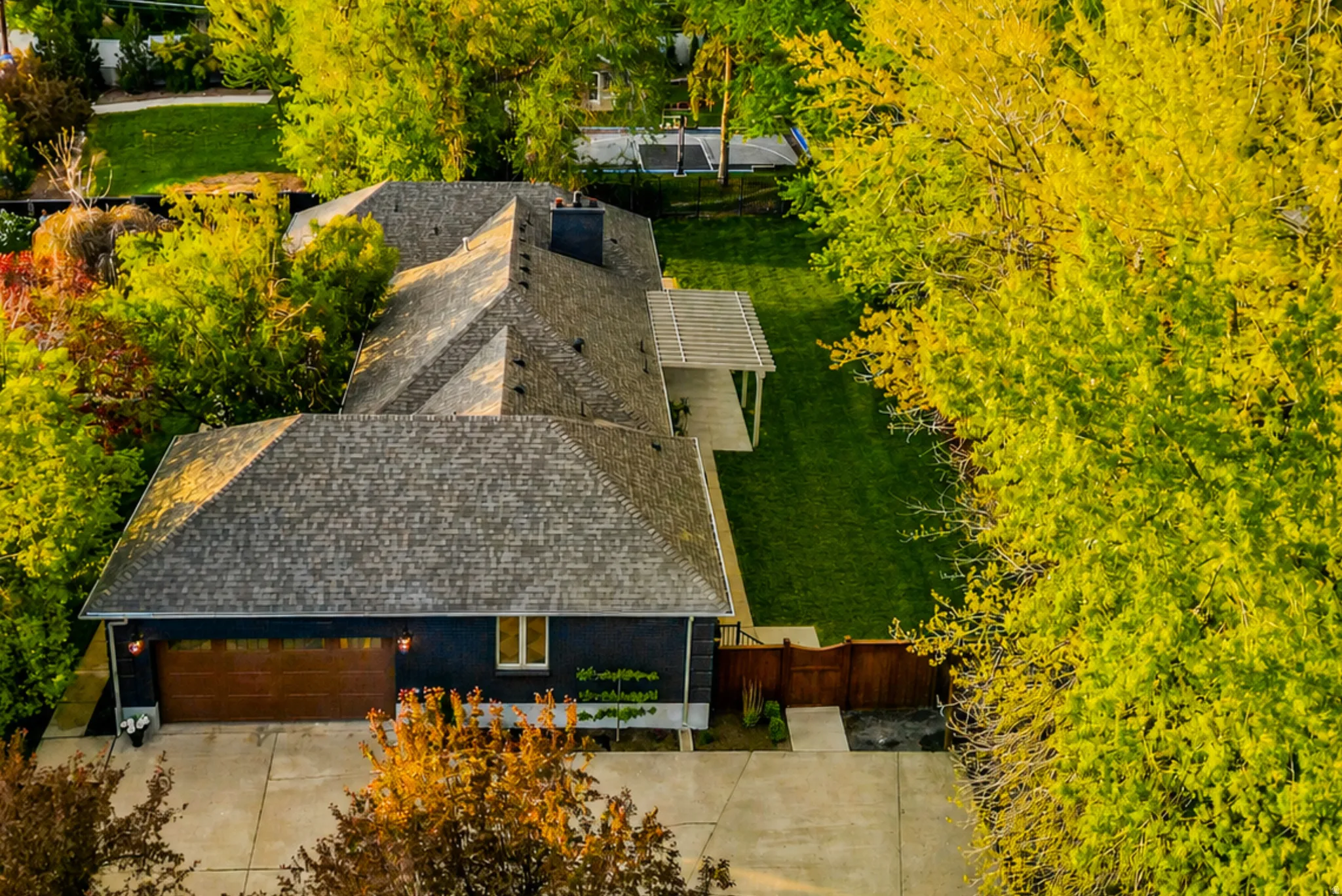 Contemporary residence featuring a dark-toned exterior with a wood-finish garage door, a prominent shingle roofline, and a concrete driveway