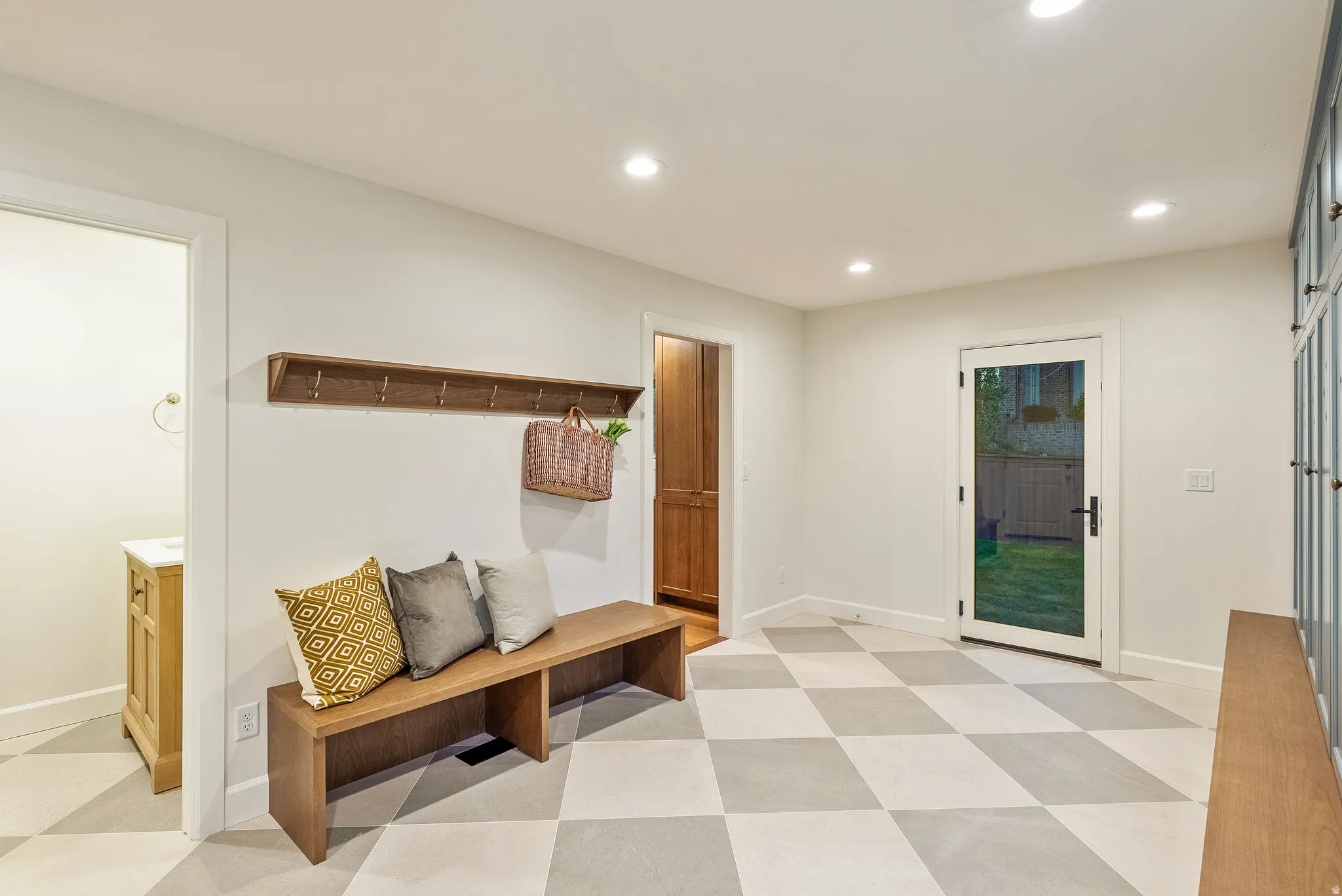 Spacious room featuring checkered flooring, recessed lighting, a built-in wooden bench with shelving, and a full-light exterior door