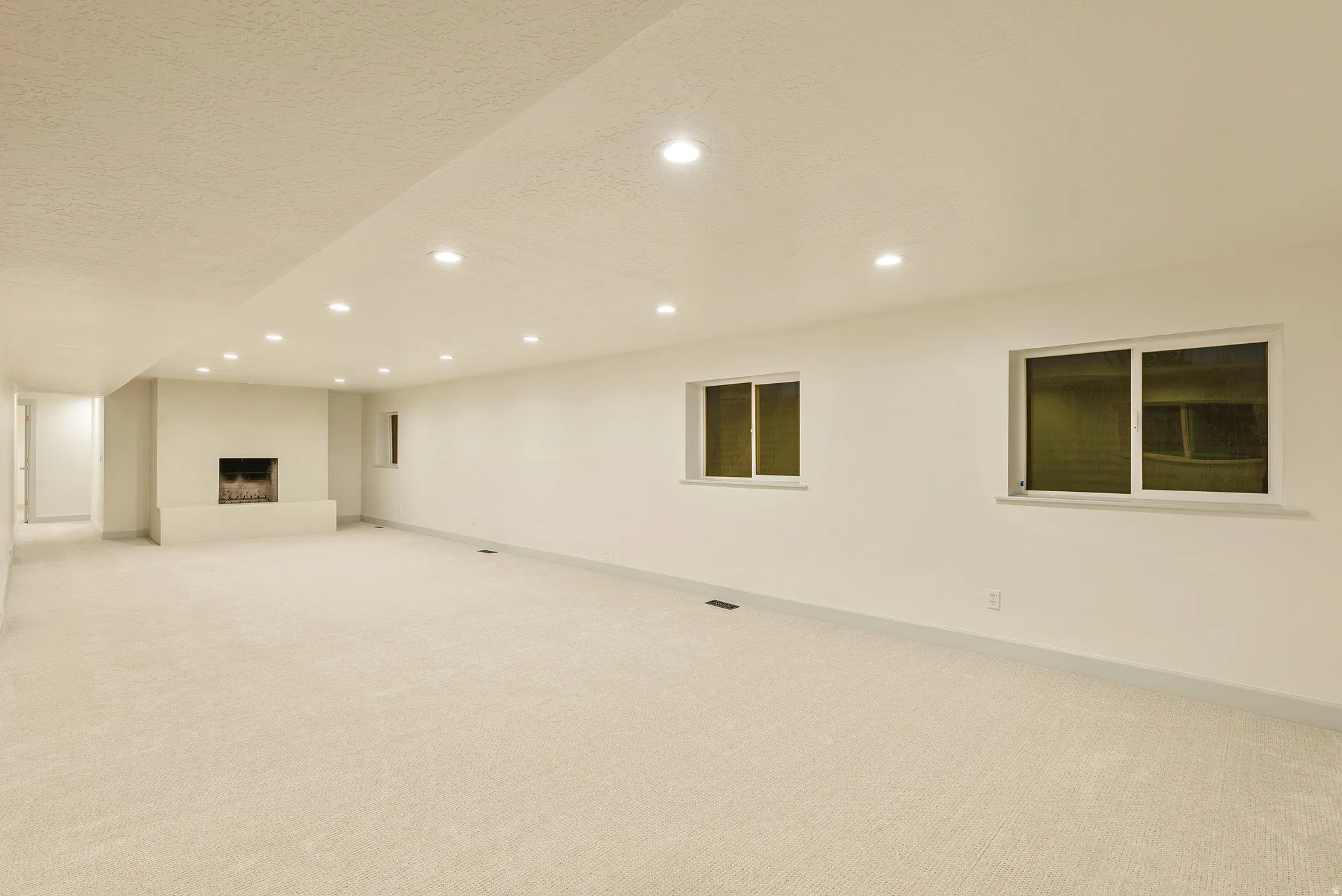 Expansive carpeted room featuring a built-in fireplace with a hearth, multiple recessed ceiling lights, and two windows