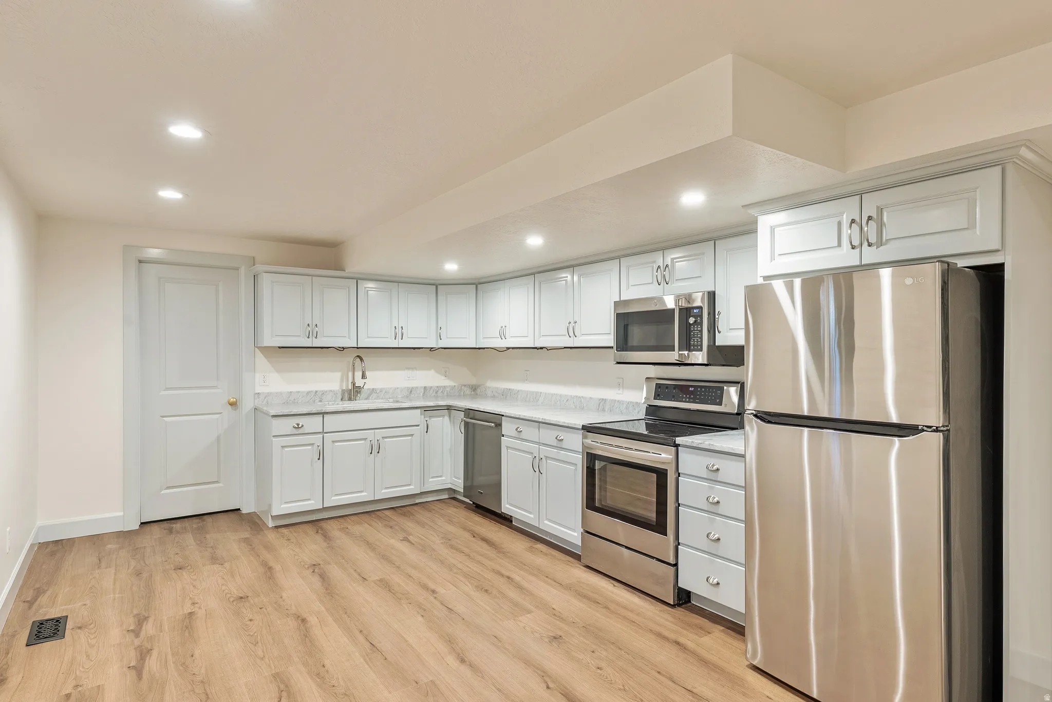 U-shaped kitchen with light-toned cabinetry, stainless steel appliances, and wood-finish flooring