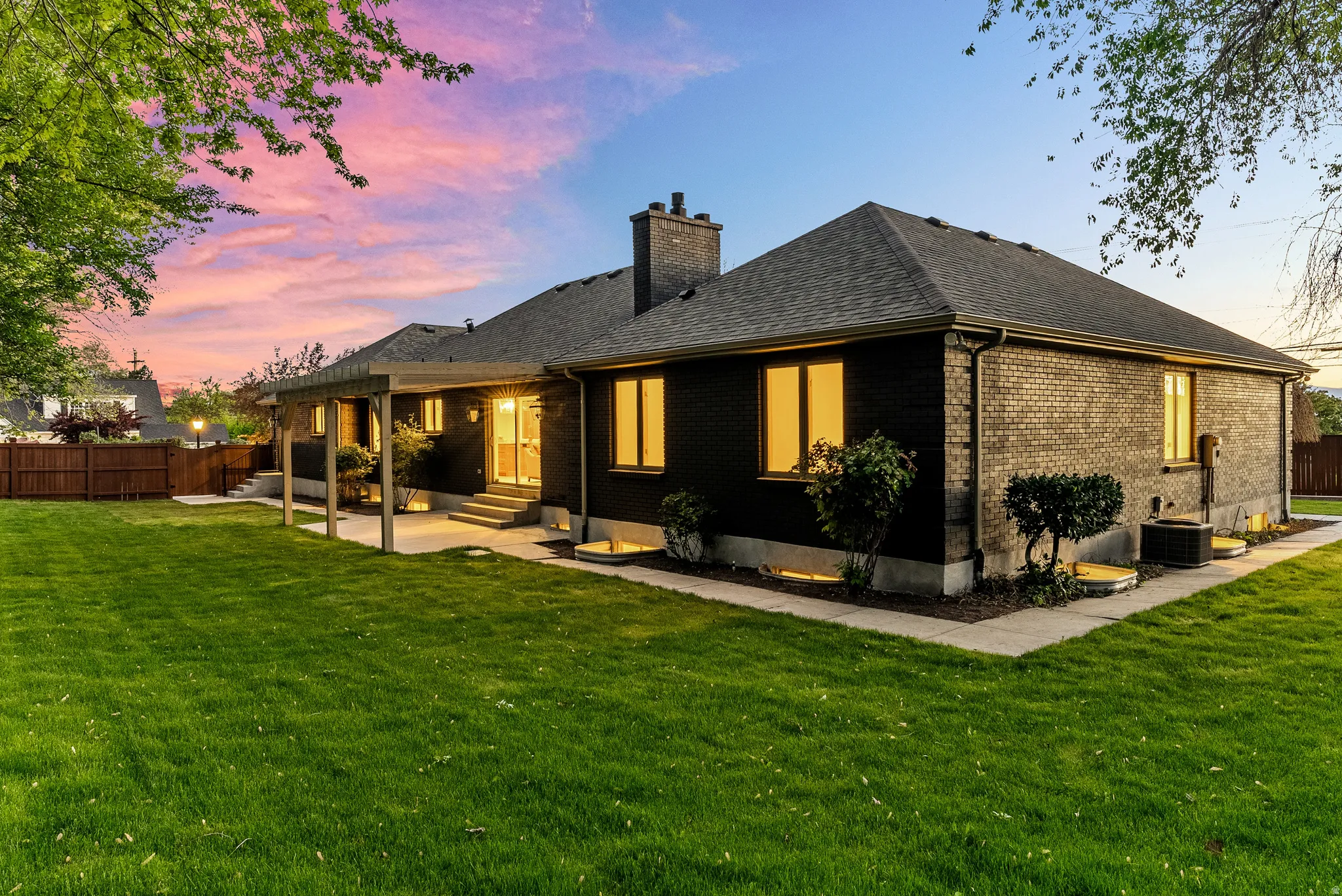 Expansive backyard featuring a large green lawn, a covered patio area, and a dark brick exterior