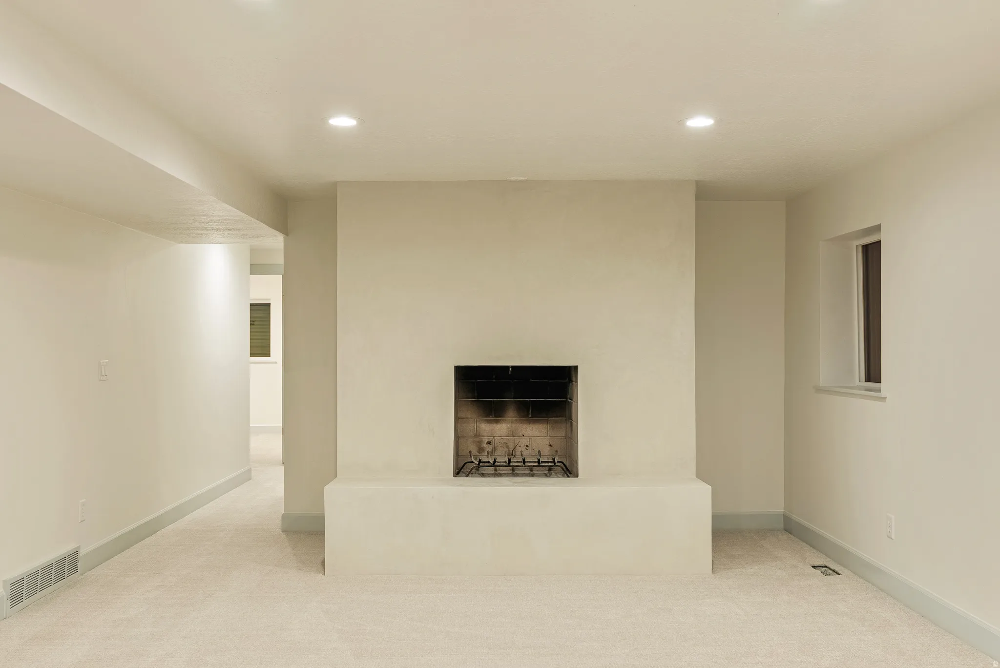 Room featuring a fireplace with a light-colored stucco finish, soft neutral carpeting, recessed lighting, and a window providing natural illumination