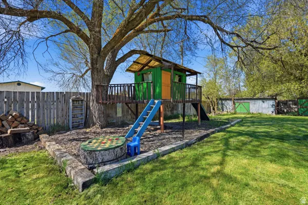 Spacious backyard featuring a built-in treehouse with a slide, a large mature tree, a wood privacy fence, a dedicated play area, and a lush green lawn