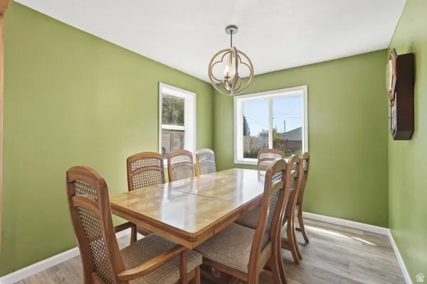 Dining area featuring two windows with white trim, wood-finish flooring, a modern chandelier, and light green painted walls