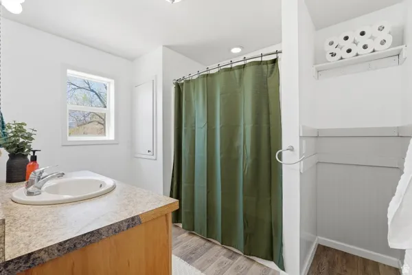 Bathroom featuring a single vanity with a laminate countertop, a window with outdoor scenery, wood-finish flooring, a shower area with a curtain, and wainscoting